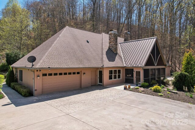 view of front of property featuring a garage, a sunroom, a chimney, and driveway
