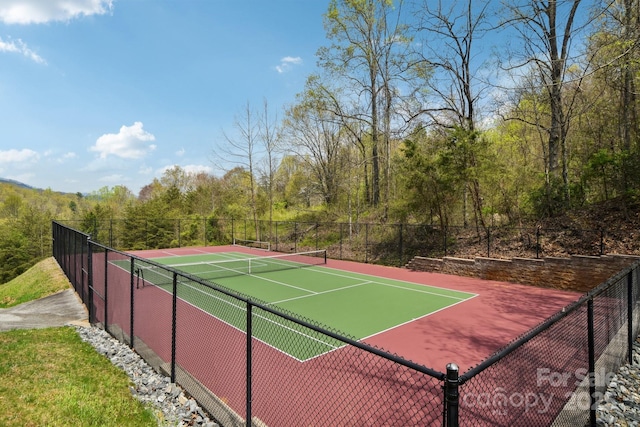 view of sport court featuring fence and a view of trees