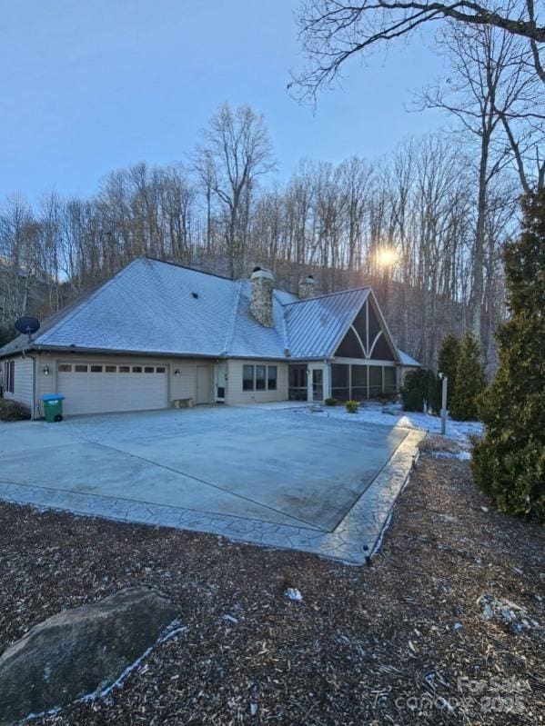 back of house featuring an attached garage, a chimney, and concrete driveway