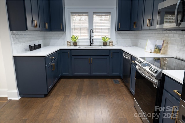 kitchen featuring blue cabinetry, light countertops, appliances with stainless steel finishes, dark wood-style floors, and a sink