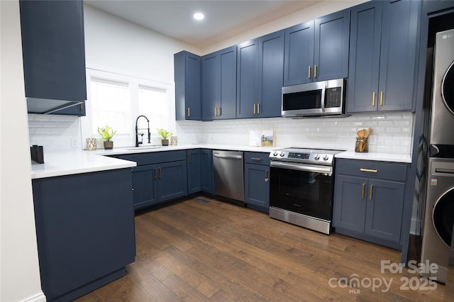 kitchen with stacked washer / dryer, blue cabinetry, dark wood-type flooring, light countertops, and stainless steel appliances