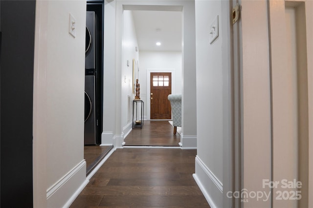 corridor with dark wood finished floors, recessed lighting, stacked washer and clothes dryer, and baseboards