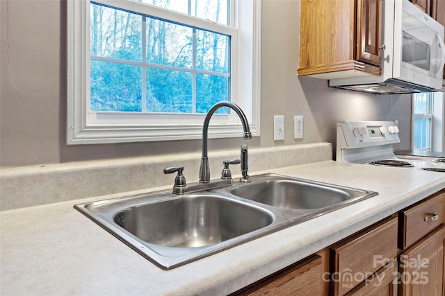 kitchen featuring brown cabinetry, white appliances, light countertops, and a sink