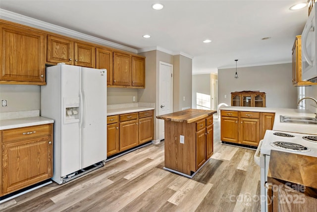 kitchen featuring white appliances, brown cabinetry, ornamental molding, a sink, and light wood-style floors