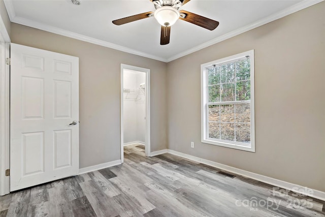 unfurnished bedroom with light wood finished floors, visible vents, a walk in closet, crown molding, and baseboards