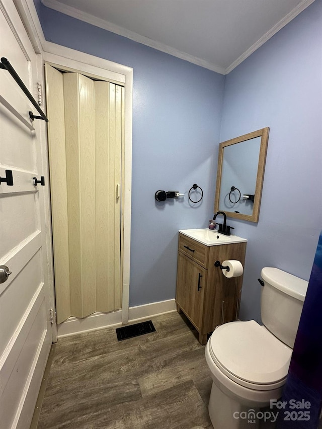 bathroom featuring vanity, wood finished floors, baseboards, ornamental molding, and toilet