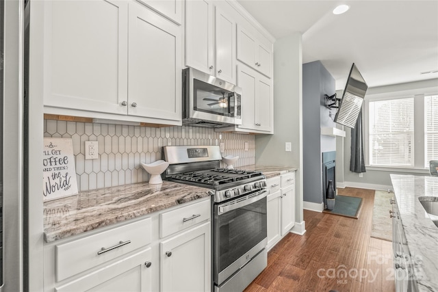 kitchen featuring dark wood finished floors, decorative backsplash, appliances with stainless steel finishes, white cabinetry, and baseboards