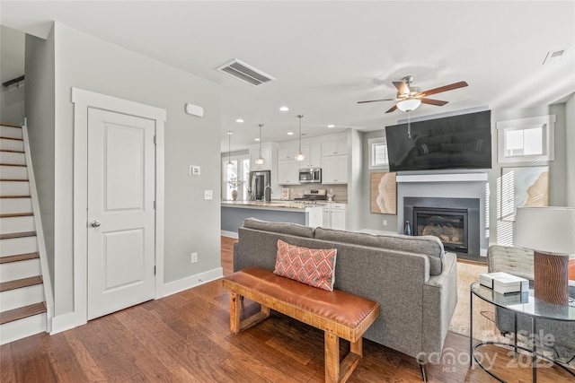 living room featuring stairs, a glass covered fireplace, wood finished floors, and visible vents