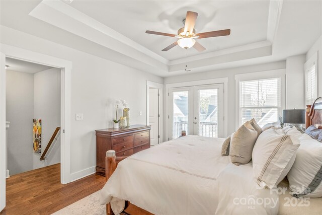 bedroom with baseboards, a raised ceiling, wood finished floors, access to exterior, and french doors