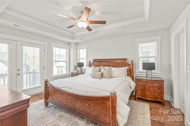 bedroom featuring light wood-style floors, a raised ceiling, a ceiling fan, and access to exterior