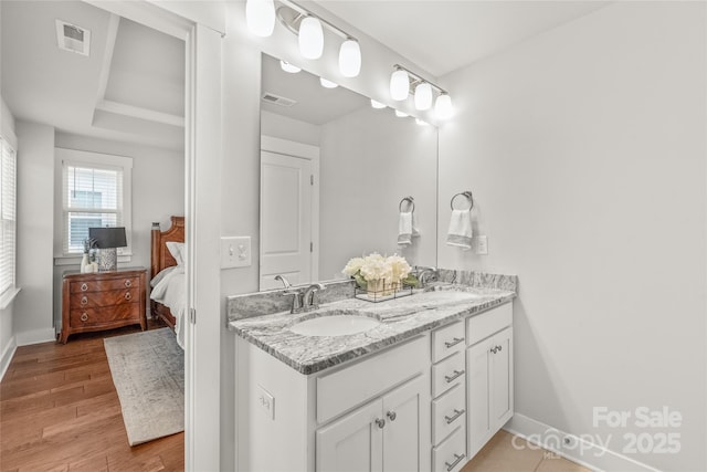 full bath with double vanity, baseboards, connected bathroom, wood finished floors, and a sink