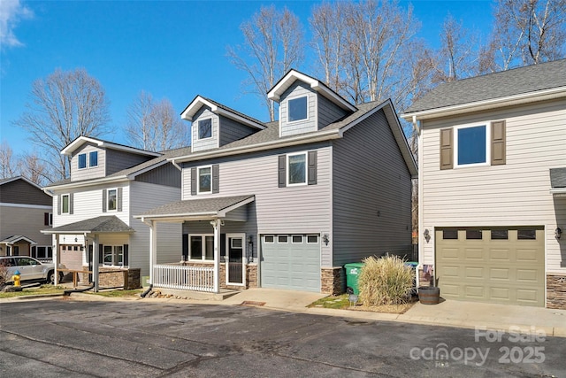 view of front of property featuring driveway, stone siding, roof with shingles, an attached garage, and covered porch