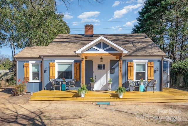 view of front of property with a shingled roof, fence, a chimney, and stucco siding