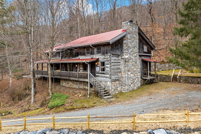 exterior space with a chimney, a porch, metal roof, fence, and a wooded view