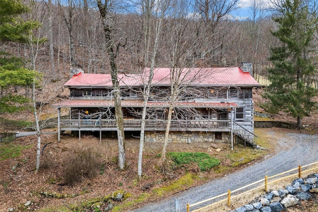 rear view of house featuring dirt driveway, a view of trees, a chimney, stairway, and metal roof