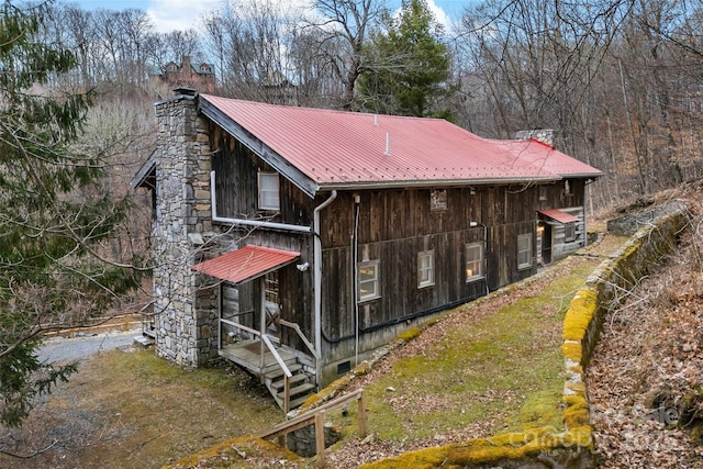 view of side of home featuring metal roof, crawl space, and a chimney