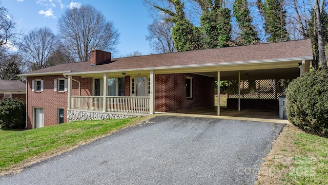 single story home featuring brick siding, a chimney, a front yard, a carport, and driveway