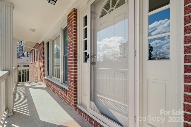 view of exterior entry with a porch and brick siding