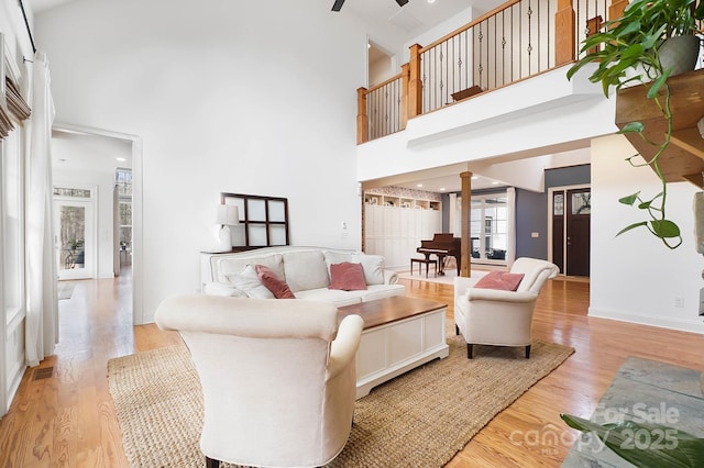 living room featuring light wood finished floors, ceiling fan, a high ceiling, and ornate columns