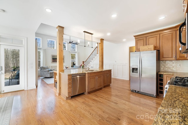 kitchen with stainless steel appliances, light wood-style flooring, brown cabinetry, a sink, and light stone countertops