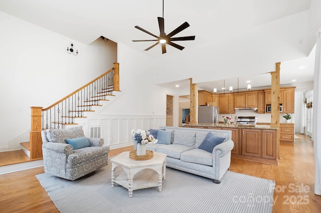 living room featuring high vaulted ceiling, recessed lighting, a decorative wall, stairs, and light wood finished floors