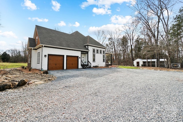 view of front of house with an outbuilding, gravel driveway, a shingled roof, an attached garage, and a shed