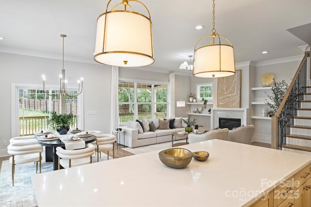 dining room featuring built in shelves, ornamental molding, stairway, an inviting chandelier, and a premium fireplace