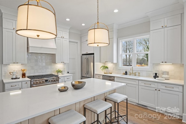 kitchen featuring a breakfast bar, a sink, light countertops, custom range hood, and high quality appliances