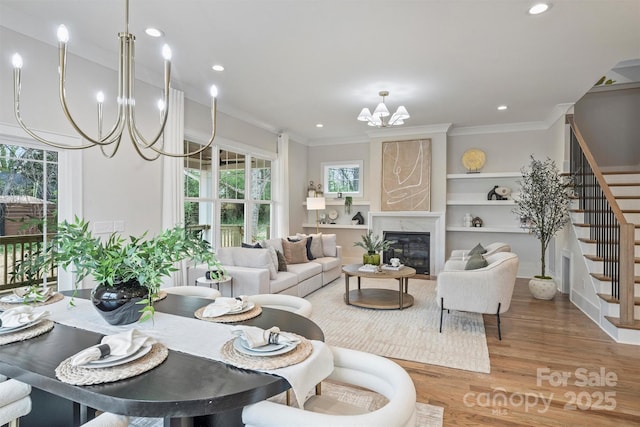 dining area with built in shelves, wood finished floors, an inviting chandelier, crown molding, and stairs