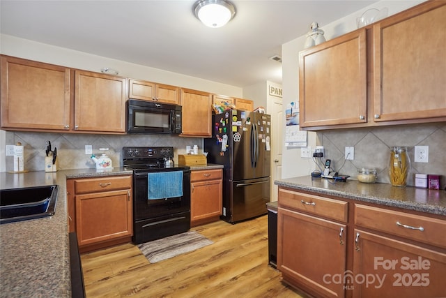 kitchen with light wood-style floors, dark countertops, backsplash, black appliances, and a sink