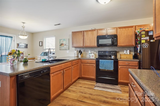 kitchen featuring visible vents, light wood-style flooring, a sink, a peninsula, and black appliances