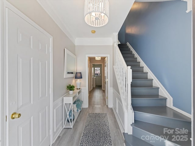 foyer entrance with a wainscoted wall, ornamental molding, wood finished floors, stairs, and a chandelier