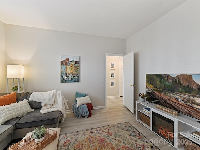 living area with light wood-style flooring, baseboards, and a glass covered fireplace