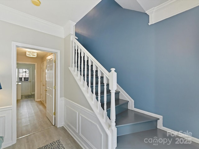 stairs with ornamental molding, wainscoting, wood finished floors, and a decorative wall