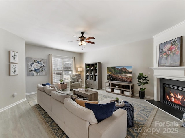 living room featuring ceiling fan, wood finished floors, a glass covered fireplace, and baseboards