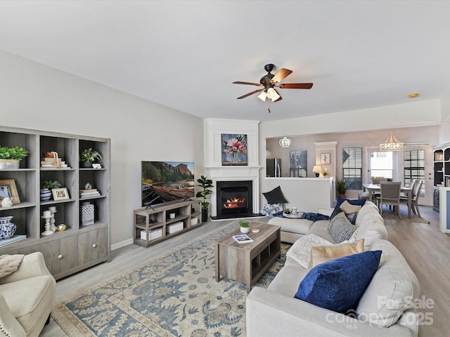 living room featuring ceiling fan, a glass covered fireplace, and wood finished floors