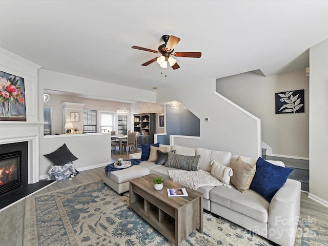 living room featuring a glass covered fireplace, ceiling fan, baseboards, and wood finished floors