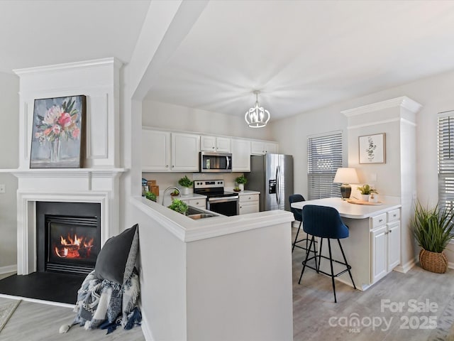 kitchen with appliances with stainless steel finishes, a peninsula, light wood-style floors, a kitchen bar, and a sink