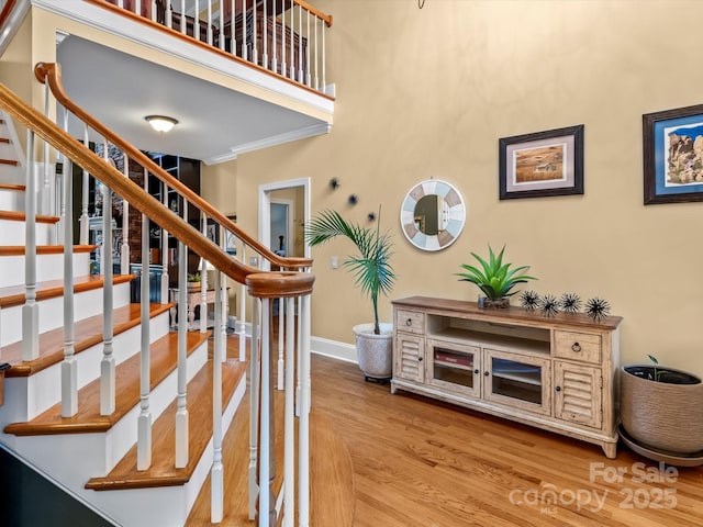 staircase with a towering ceiling, baseboards, wood finished floors, and ornamental molding