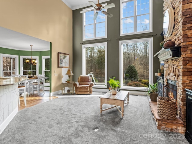 living room with ceiling fan with notable chandelier, a high ceiling, a fireplace, baseboards, and ornamental molding