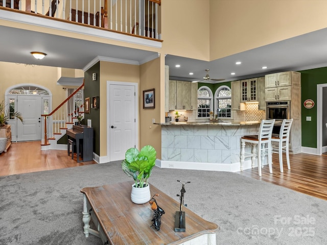 carpeted living room with crown molding, stairway, a high ceiling, wood finished floors, and baseboards