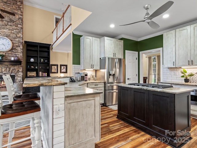 kitchen with light wood finished floors, appliances with stainless steel finishes, ornamental molding, a ceiling fan, and a peninsula