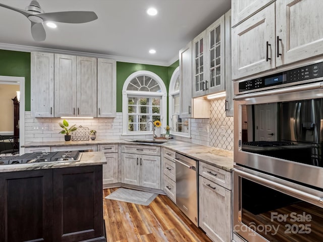 kitchen with light stone counters, appliances with stainless steel finishes, ornamental molding, a sink, and light wood-type flooring