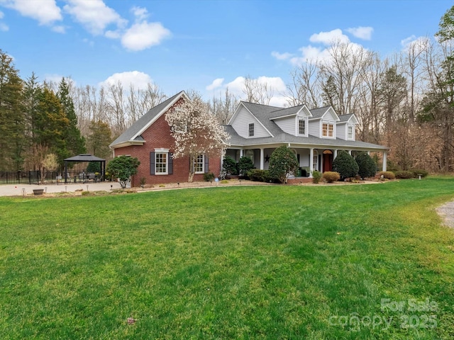 view of front of property with brick siding, covered porch, a gazebo, fence, and a front lawn