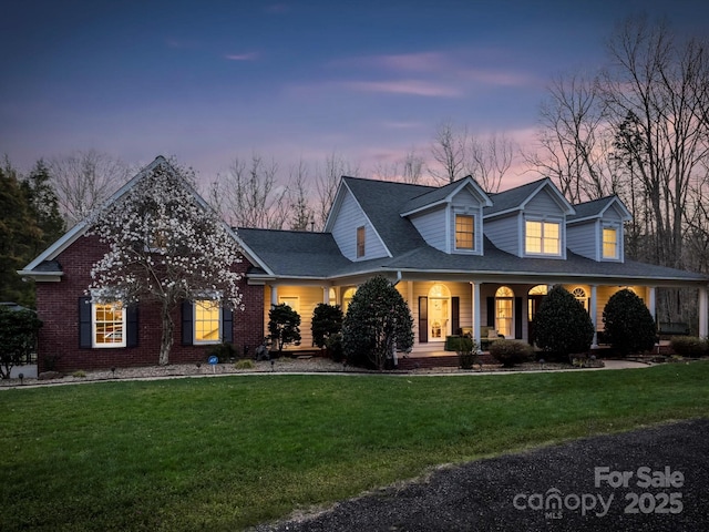 view of front of home featuring a shingled roof, brick siding, and a yard