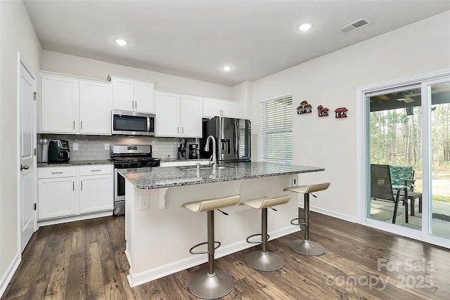 kitchen featuring stainless steel appliances, visible vents, dark wood-type flooring, a sink, and dark stone counters