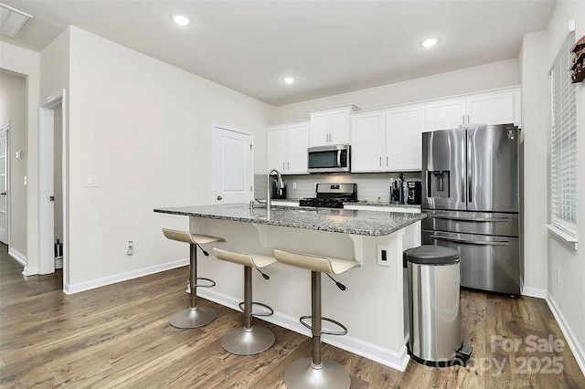 kitchen with dark stone counters, decorative backsplash, an island with sink, stainless steel appliances, and a kitchen bar