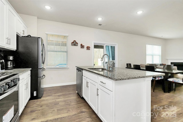 kitchen with stainless steel appliances, dark wood-style flooring, dark stone countertops, and a sink