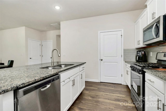 kitchen featuring stainless steel appliances, dark wood-type flooring, a sink, backsplash, and dark stone countertops