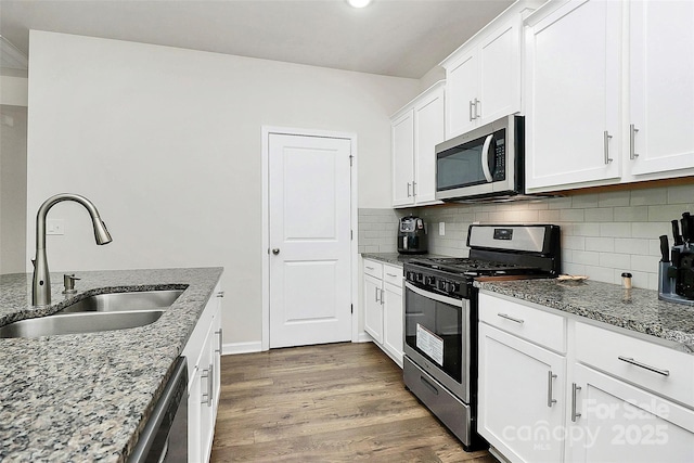 kitchen with stainless steel appliances, wood finished floors, a sink, decorative backsplash, and dark stone counters